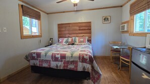 Ein Schlafzimmer mit hölzernem Kopfteil, einem Bett mit kariertem Bettbezug, einem Schreibtisch mit Stuhl und einem Kühlschrank.