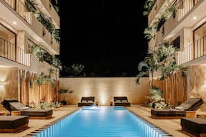 A poolside area with lounge chairs, a swimming pool, and plants. - Majaro Apartments (Tulum)