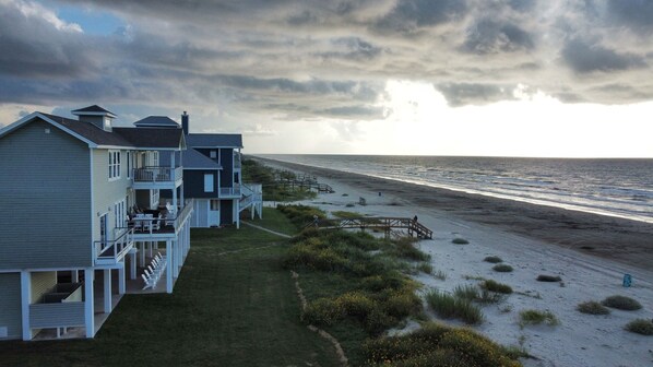 A beachfront property with multiple-story buildings, a wooden deck, and a pathway leading to the beach.