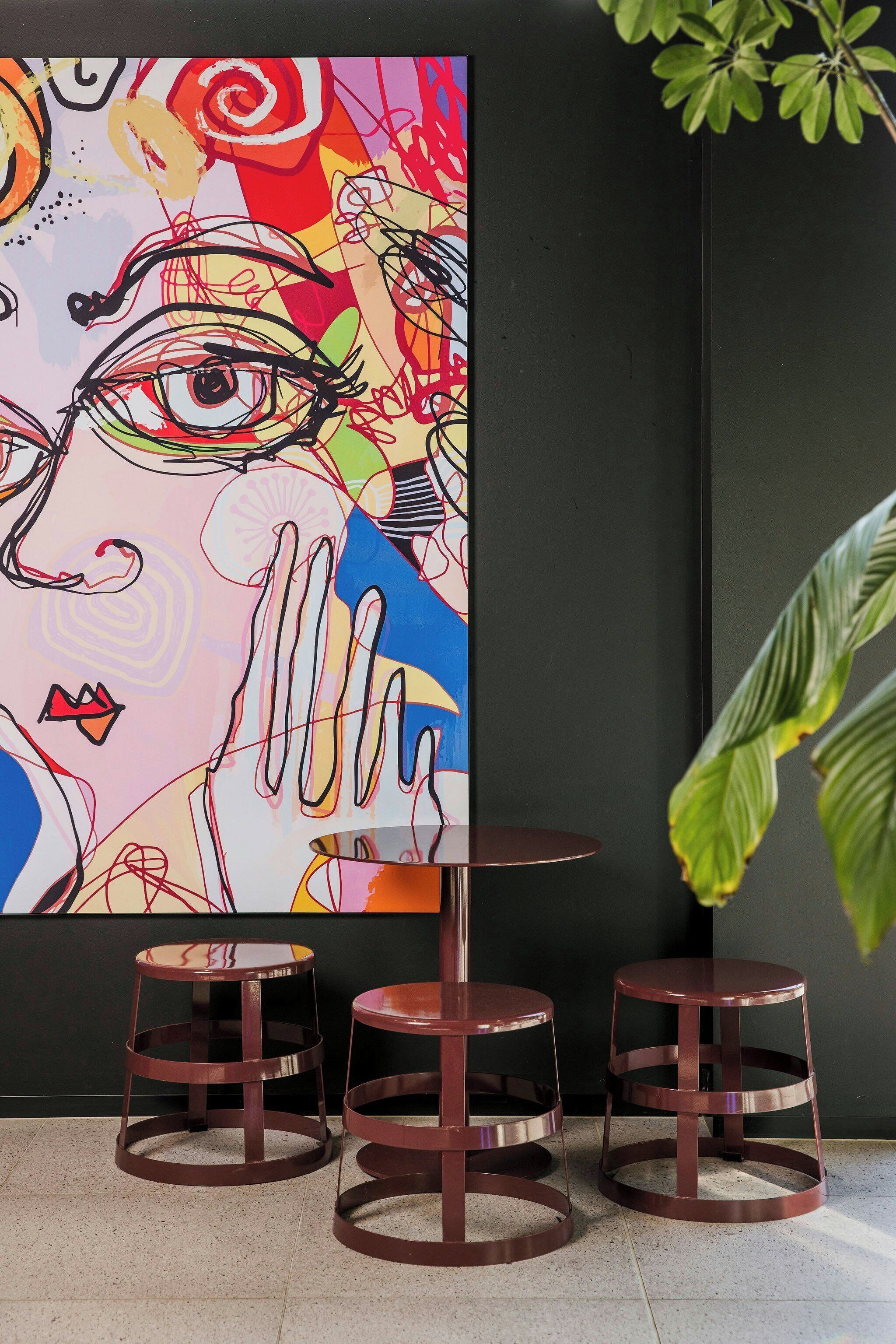 A modern interior with a colorful abstract painting, a round table, and two stools.