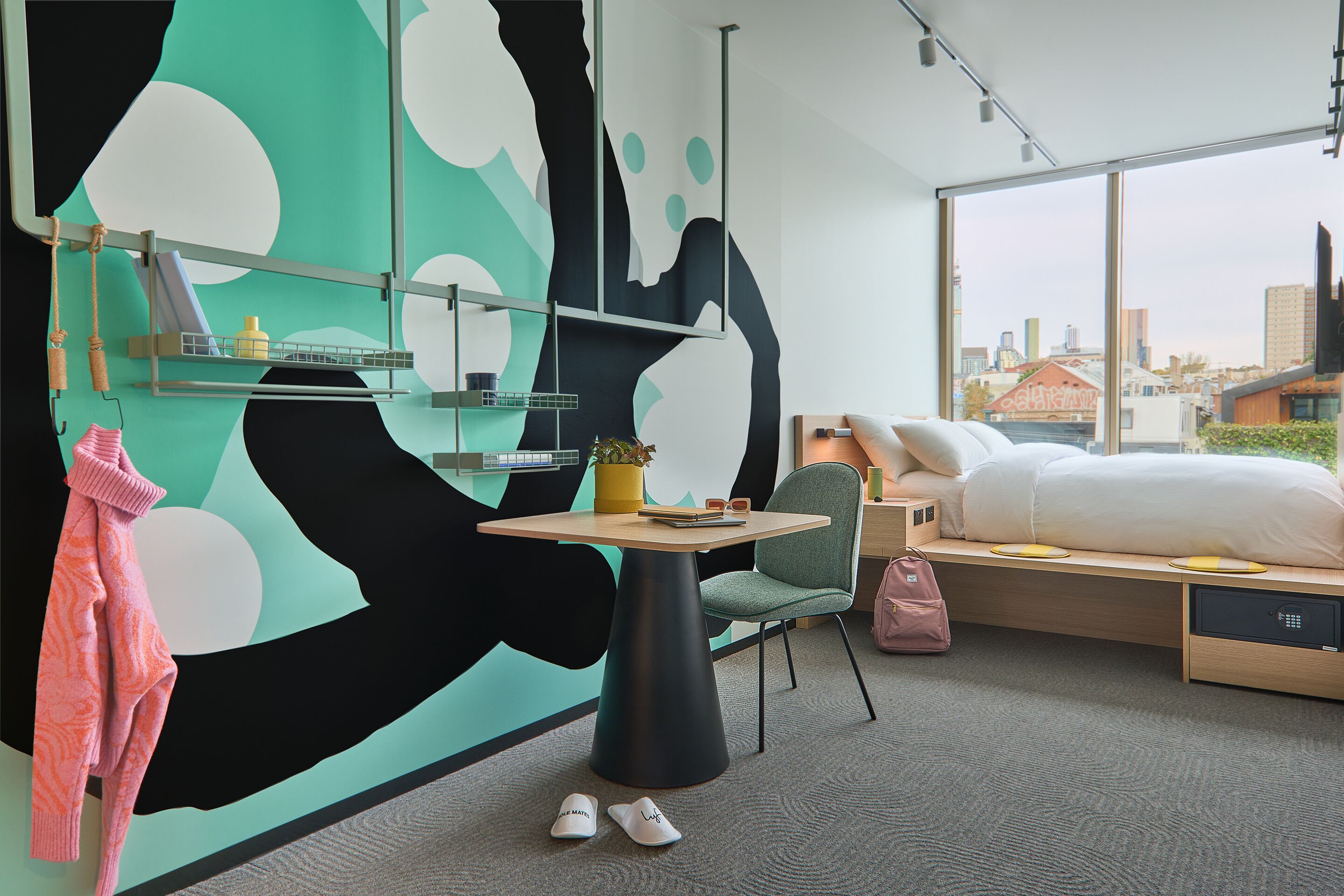 Quarto de hotel moderno com uma janela grande, uma cama, uma mesa e uma cadeira.