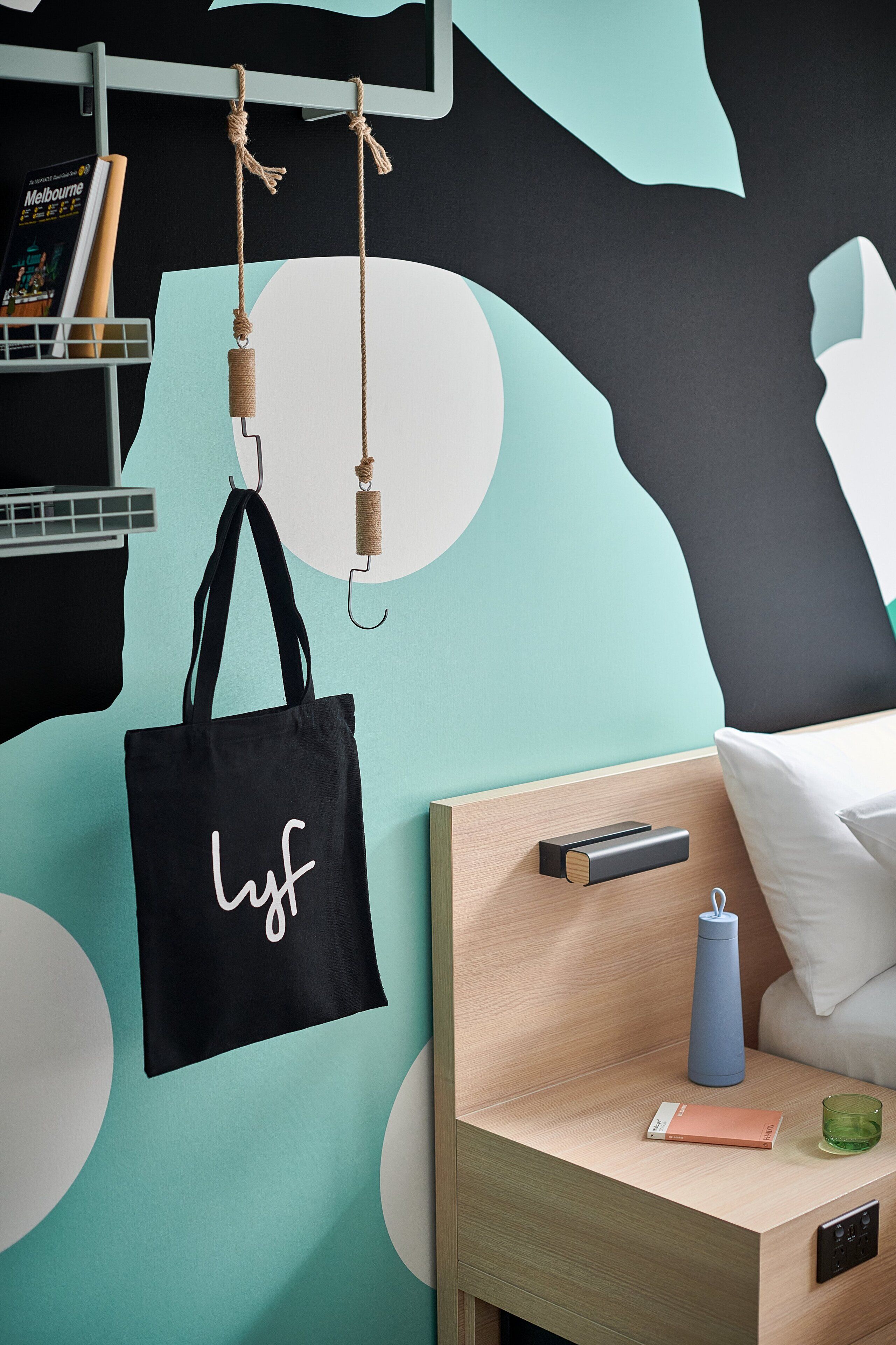 A neatly organized bedroom with a bed, bedside table, and a wall with abstract art.