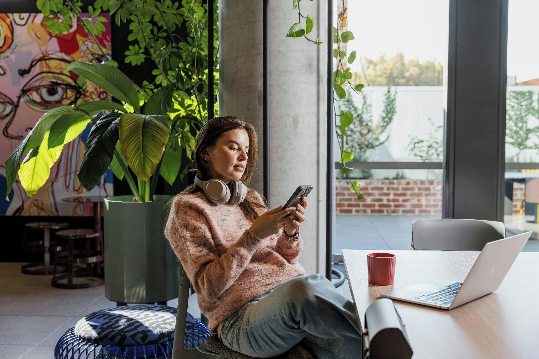 Una persona sentada a una mesa con una computadora portátil, audífonos y un teléfono inteligente.