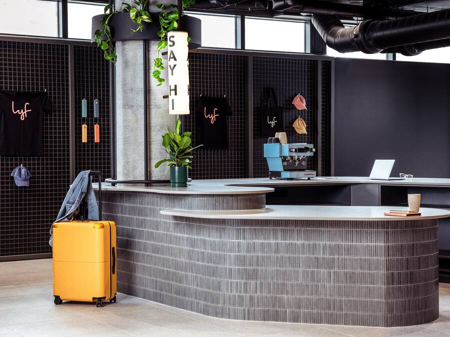 Un mostrador de recepción moderno con diseño curvo, una planta en maceta y un cartel que dice "SAY HI".