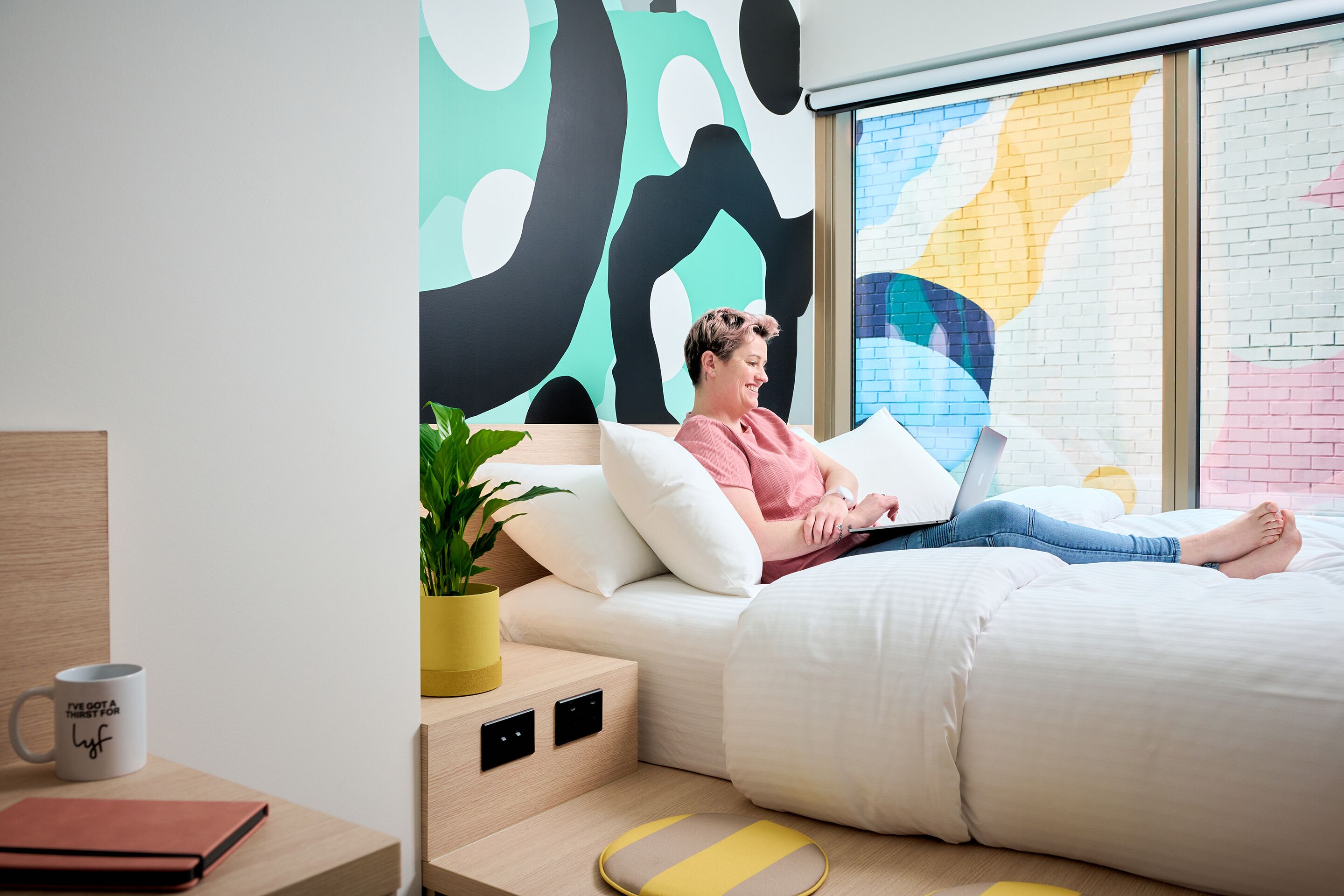 A modern bedroom with a bed, a laptop, and a potted plant.