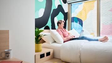 A modern bedroom with a bed, a laptop, and a potted plant.