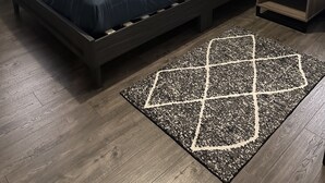 A neatly arranged bedroom with a bed, bedside table, lamp, and a decorative rug.