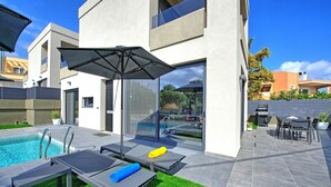 A modern outdoor pool area with lounge chairs, a barbecue, and a glass-enclosed patio.