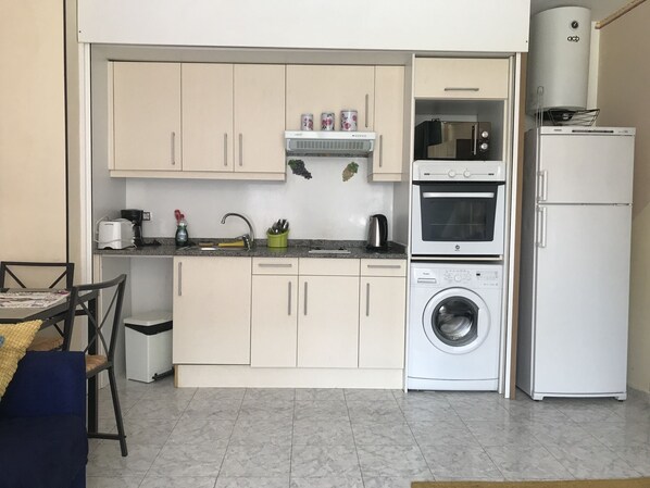 A compact kitchen with a washing machine, a microwave, and a refrigerator.