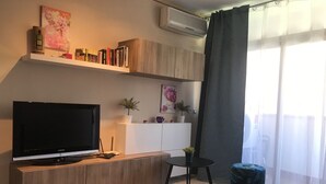 Ett modernt vardagsrum med en platt-TV placerad på en träkonsol, ett litet runt bord och en krukväxt.