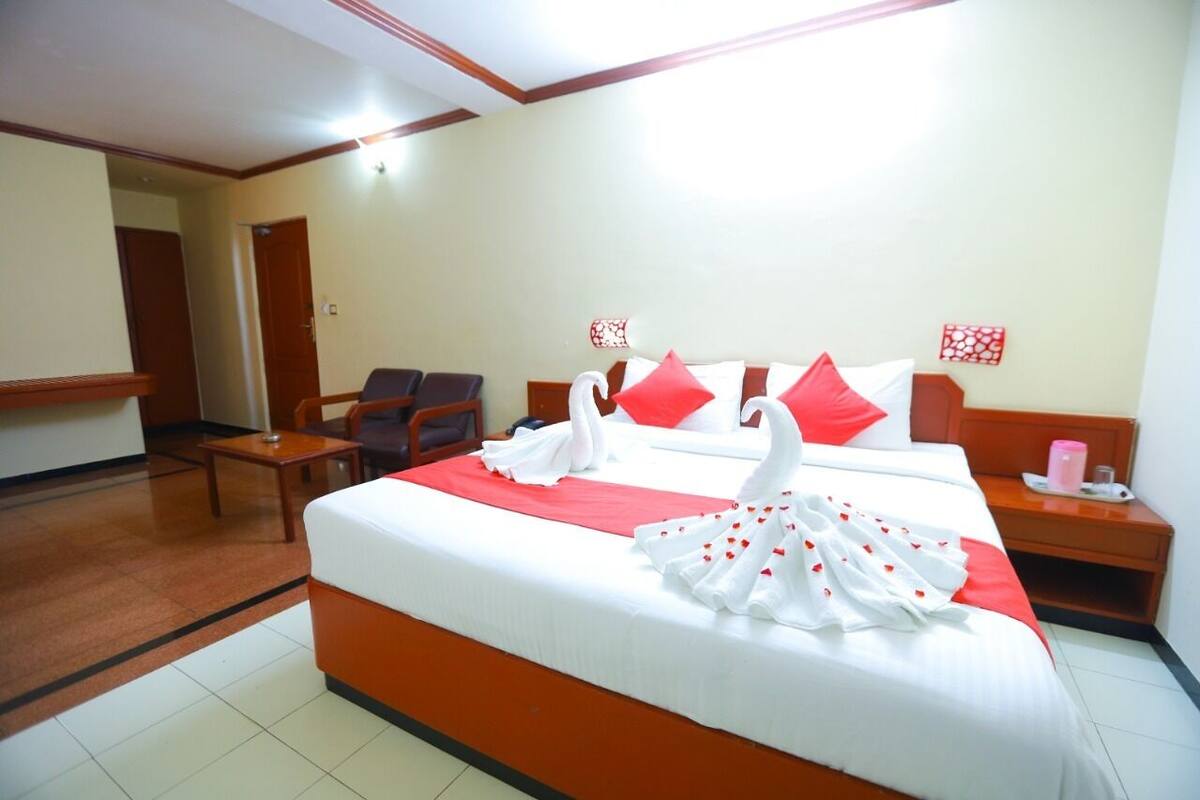 A hotel room with a large bed, two chairs, a small table, and a nightstand.