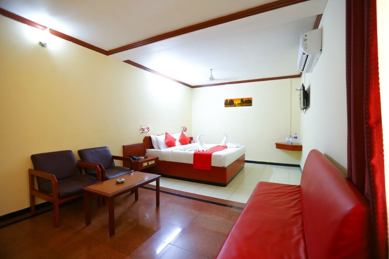 A hotel room with a bed, two armchairs, a small table, and a red sofa.