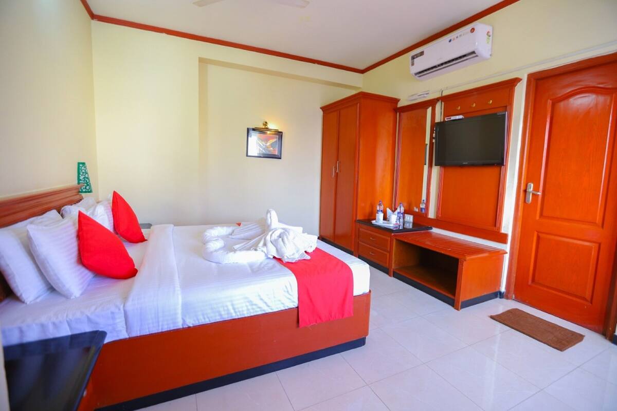 A hotel room with a bed, a TV, a wardrobe, and an air conditioning unit.