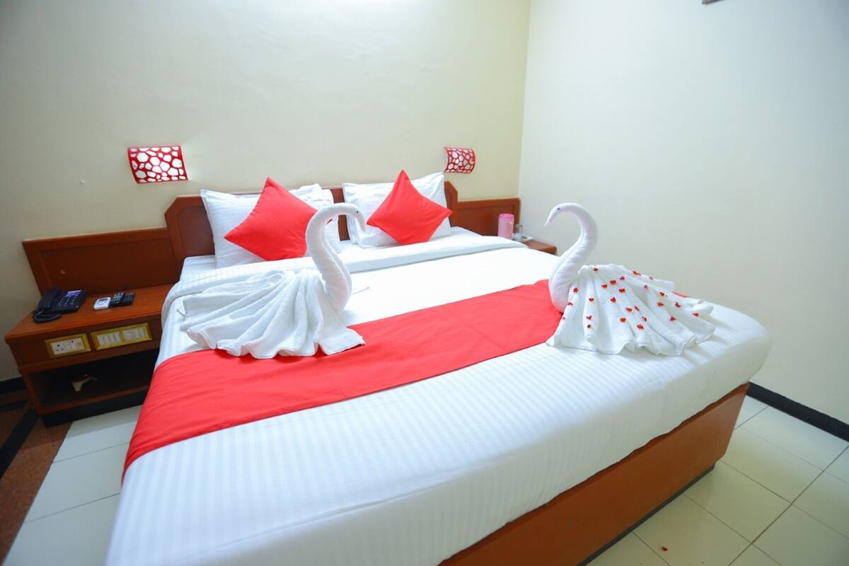 A hotel room with a large bed, red and white bedding, and decorative swan pillows.