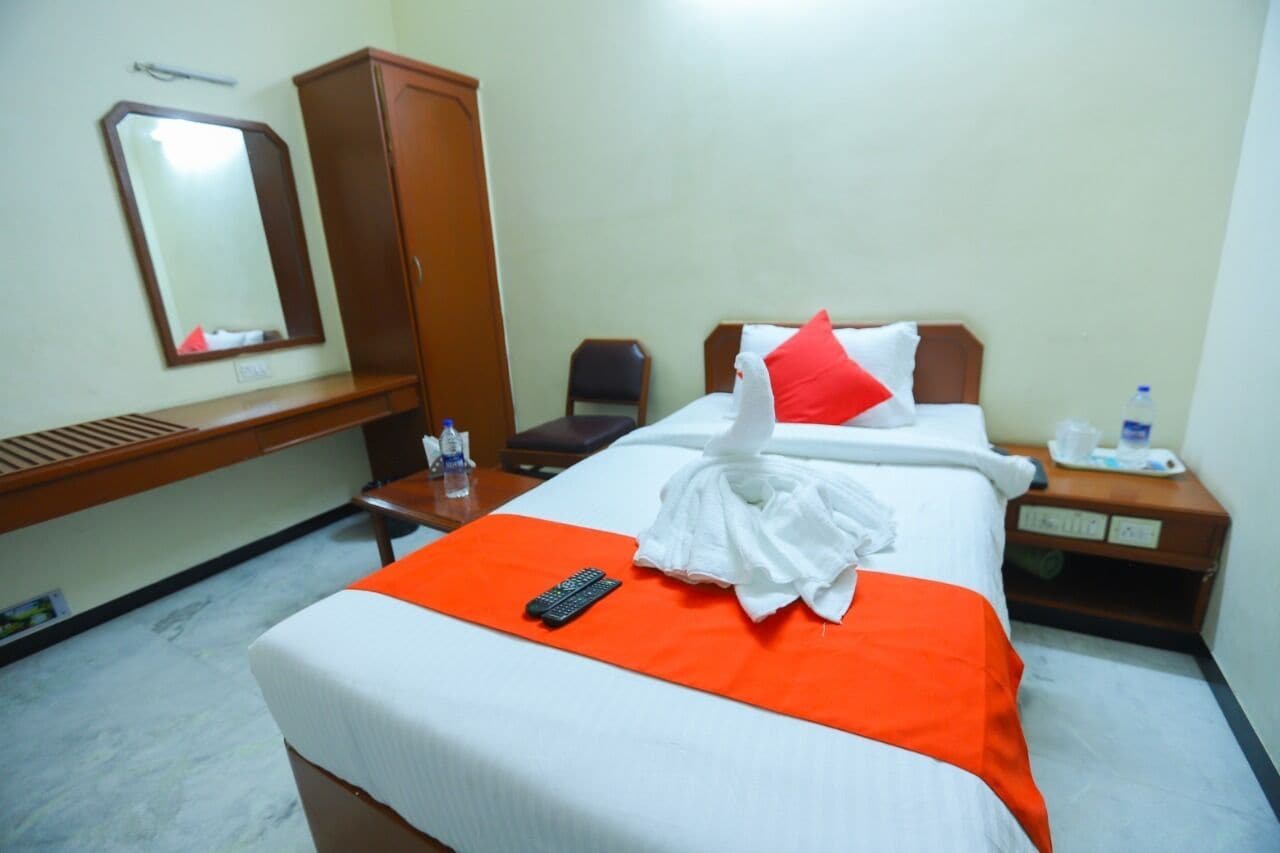 Quarto de hotel com uma cama, escrivaninha, cadeira, guarda-roupa e espelho.