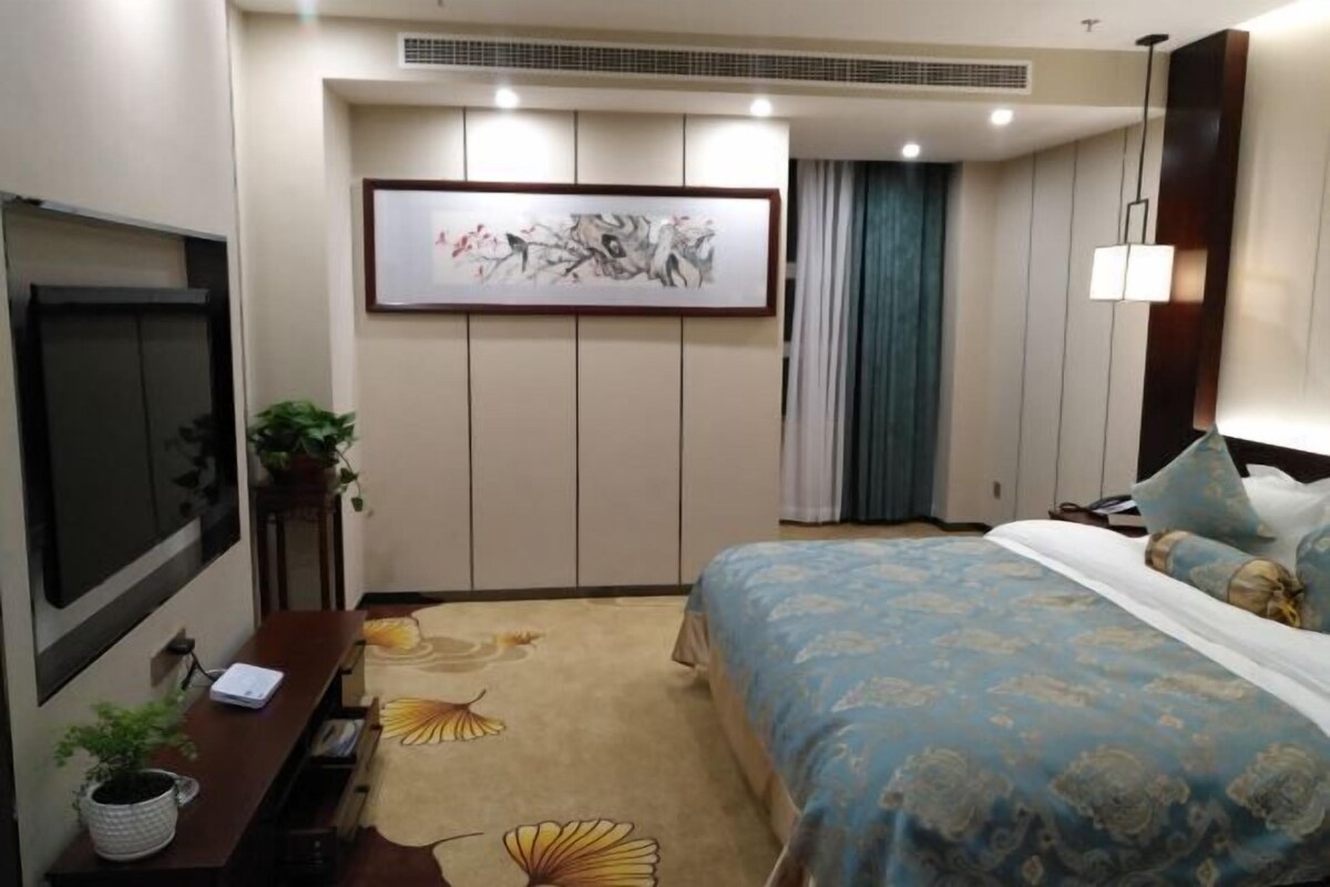 A hotel room with a bed, a desk, a TV, and a painting on the wall.