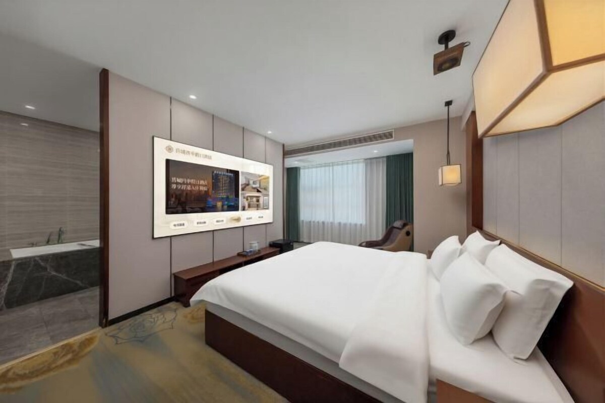 A hotel room with a large bed, a TV mounted on the wall, a desk, and a bathroom with a bathtub.
