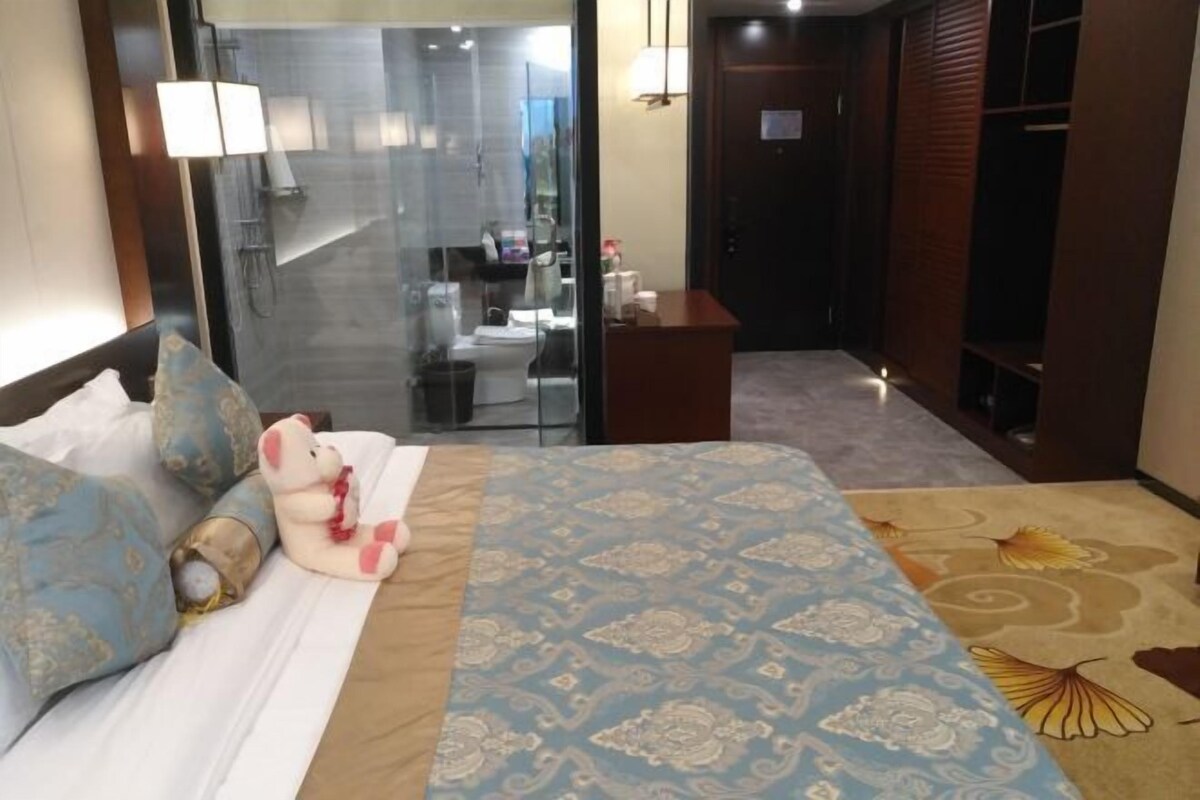 A hotel room with a bed, a glass shower area, a desk, and a wardrobe.