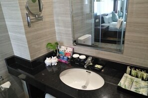 Une salle de bain moderne avec un plan de toilette noir, un lavabo blanc et un grand miroir. On y trouve des articles de toilette et une plante sur le plan de toilette.