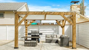 Eine überdachte Terrasse im Freien mit Grill, Korbmöbeln und einem Steinkamin.