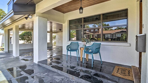 A covered patio area with two blue chairs, a small table, and a potted plant. - Mid-Century Modern Escape in Central Lakeland! (Lakeland)