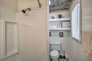 Een compacte badkamer met een douche, toilet en planken met handdoeken en planten.