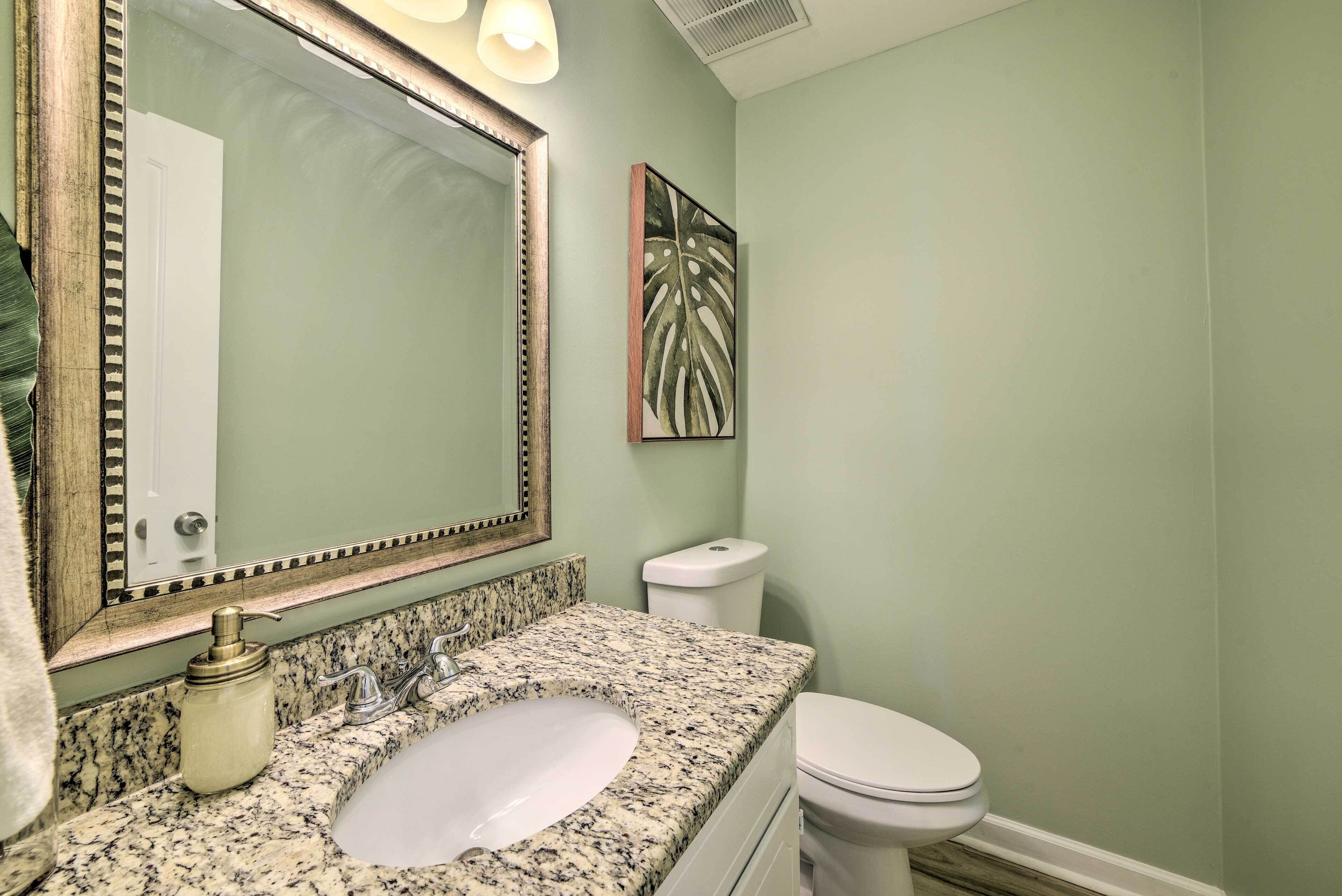 Un baño con lavamanos de encimera de granito, inodoro blanco y espejo con marco decorativo.