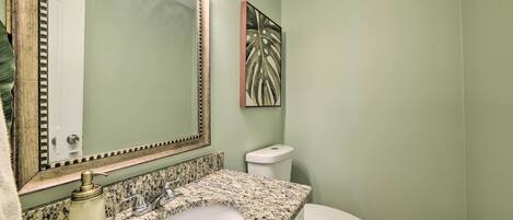 Un baño con lavamanos de encimera de granito, inodoro blanco y espejo con marco decorativo.