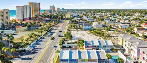 A coastal town with a prominent hotel featuring a colorful facade, a parking lot, and a view of the beach and ocean.