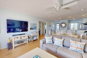 Ein geräumiges Wohnzimmer mit einem großen Flachbildfernseher, einem Deckenventilator und einem Sofa mit Strandkissen.