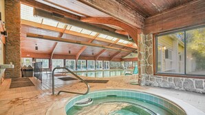 Un'ampia piscina coperta con parete in pietra e travi in legno, circondata da poltroncine relax e una porta in vetro che dà sull'esterno.