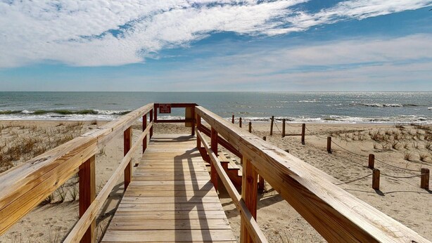 A wooden boardwalk leading to the beach with a sign indicating a lifeguard on duty.