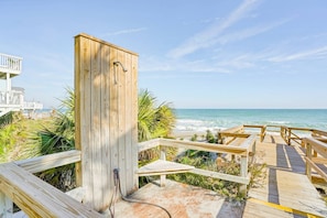 Eine Holzterrasse mit Meerblick, eine Holzkonstruktion mit einem Schlauch und ein weißes Gebäude im Hintergrund.