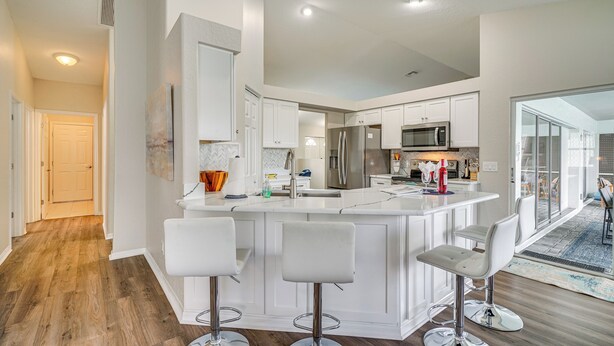 A modern kitchen with white cabinetry, stainless steel appliances, and a central island with bar stools. - 'Villa Sol Mate' - Waterfront Cape Coral Home! (Cape Coral)