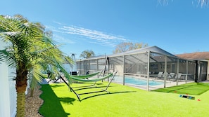 A backyard with a swimming pool, a covered seating area, and a hammock.