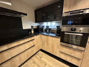 Una cucina moderna con piani di lavoro neri, mobili in legno, forno integrato e macchina per il caffè.