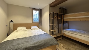 Un dormitorio con literas, cabecera de madera, mesita de noche con lámpara y ventana con vistas a la vegetación.