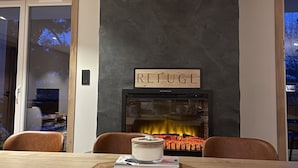 Un comedor moderno con una mesa de madera, sillas, una chimenea y un letrero que dice "REFUGE".