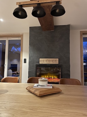 Un'area pranzo moderna con un tavolo in legno, sedie, un camino e un cartello con la scritta 'REFUGE'.