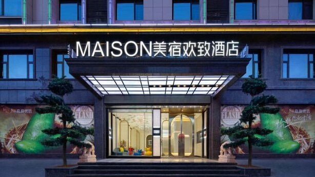 A hotel entrance with a glass facade, a sign above the entrance, and two potted plants on either side. - MAISON Hotel (Liuyang Economic Development Zone, Coach Station, Liuyang) (Liuyang)