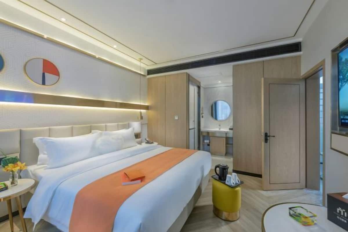 A modern hotel room with a large bed, bedside table, and a small desk.
