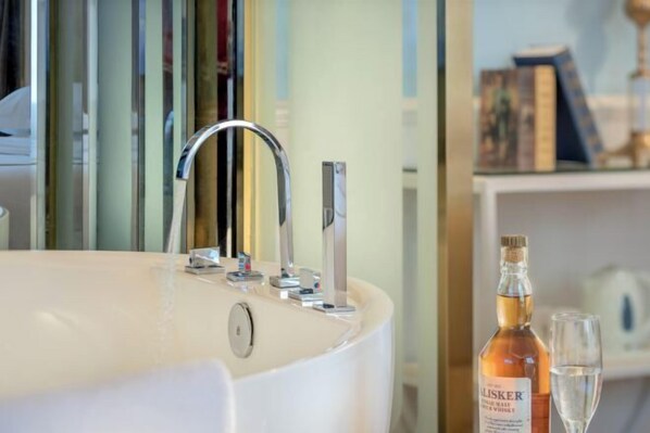 A modern bathroom with a large bathtub, a faucet, and a bottle of liquor on a shelf.