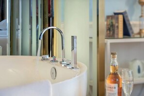 A modern bathroom with a large bathtub, a bottle of liquor, and a glass.