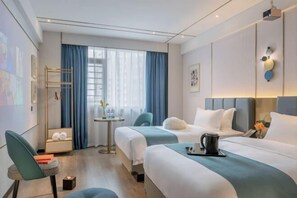A hotel room with two beds, a small table with a kettle, a chair, and a window with curtains.