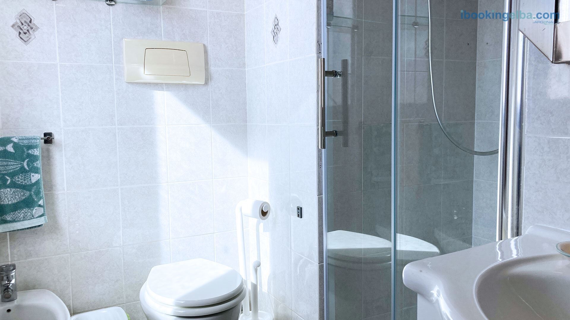 A bathroom with a glass shower enclosure, a toilet, a sink, and a towel rack with a patterned towel.