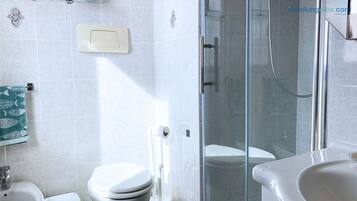 A bathroom with a glass shower enclosure, a toilet, a sink, and a towel rack with a patterned towel.