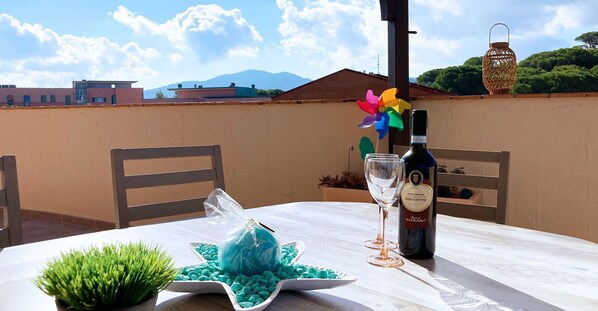 A table set outdoors with a bottle of wine, two glasses, a decorative star-shaped dish, and a small potted plant.