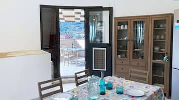 A dining area with a table set for two, a cabinet with glass doors, and a view of a balcony with outdoor furniture.