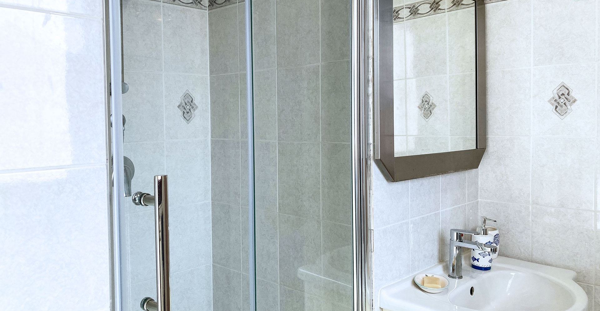 A bathroom with a glass-enclosed shower, a sink with a soap dish, and a mirror.