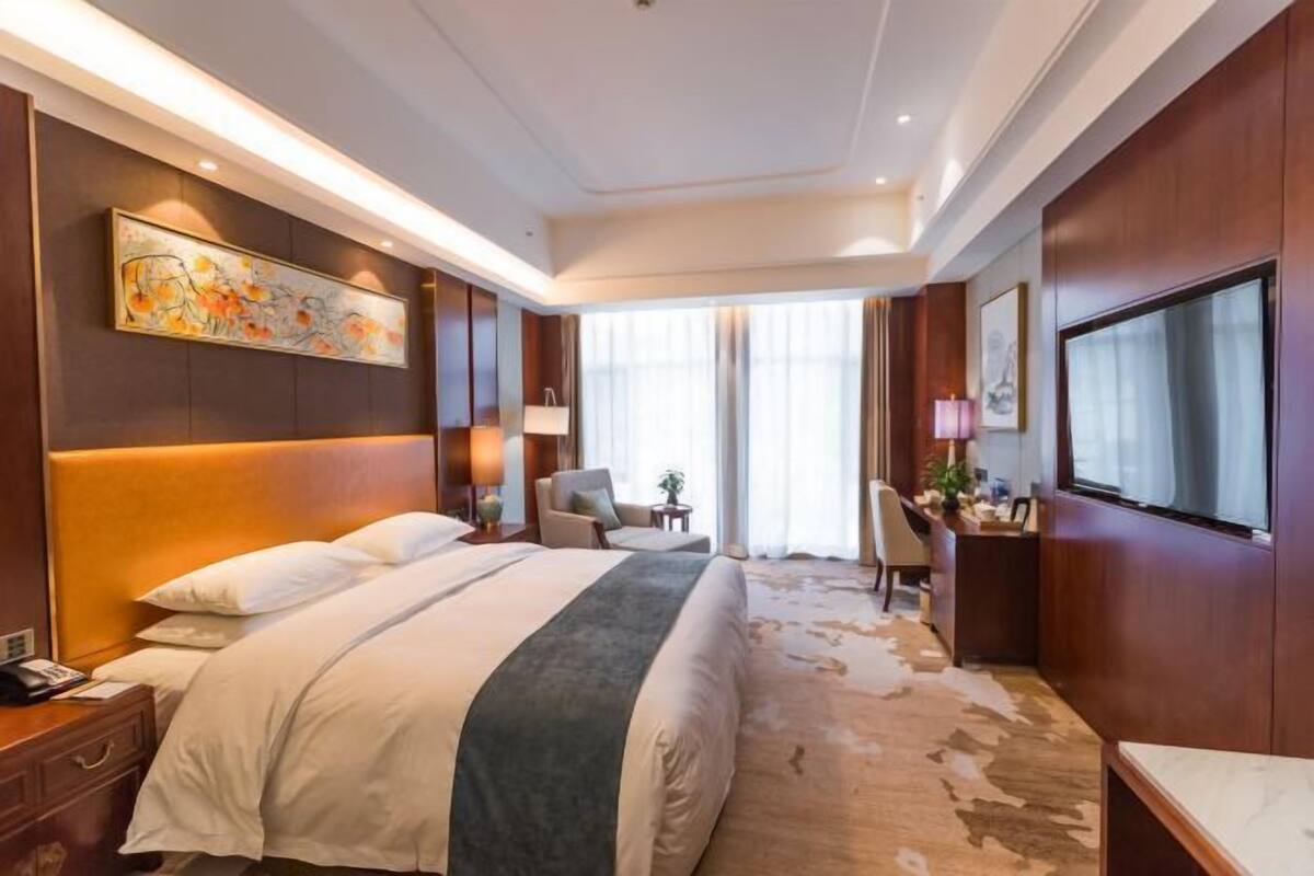 A hotel room with a large bed, a desk, a chair, a TV, and a painting on the wall.